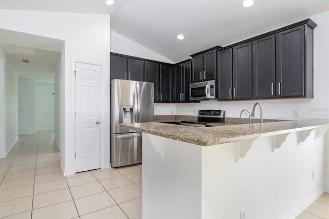 kitchen featuring stainless steel appliances, a peninsula, a breakfast bar area, light tile patterned floors, and dark cabinets