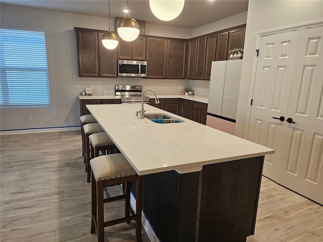 kitchen with a sink, a kitchen breakfast bar, stainless steel appliances, dark brown cabinetry, and light wood finished floors