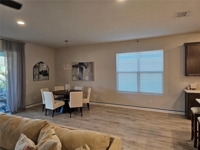 dining space featuring light wood-style flooring, baseboards, visible vents, and a textured ceiling