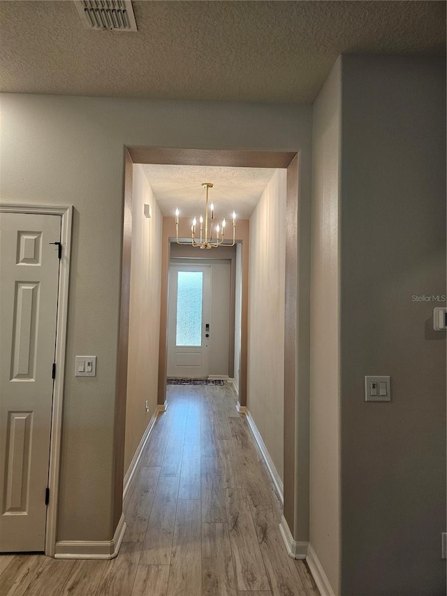 hallway featuring light wood-style flooring, baseboards, visible vents, and a textured ceiling