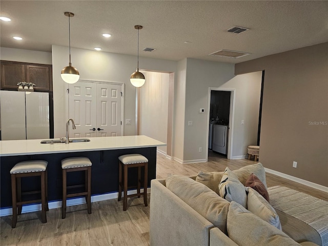 kitchen featuring visible vents, light wood-type flooring, a sink, freestanding refrigerator, and light countertops