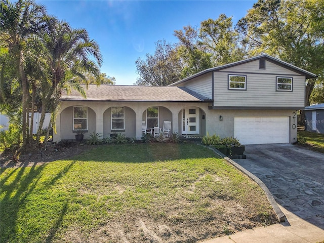 tri-level home with stucco siding, concrete driveway, covered porch, an attached garage, and a front yard