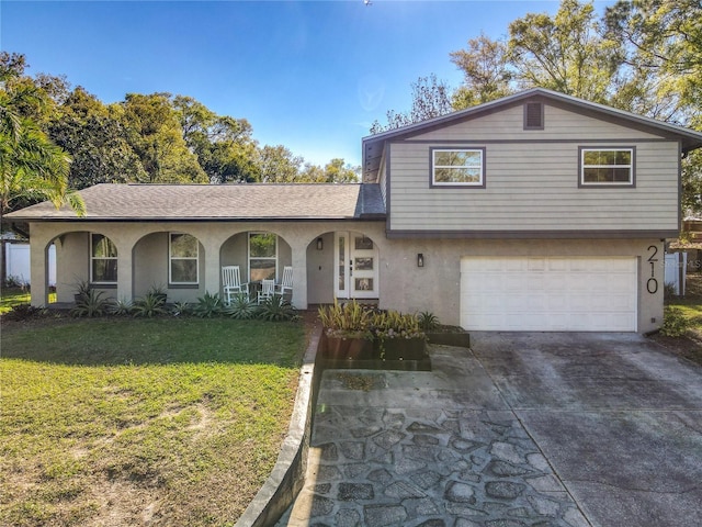 tri-level home with stucco siding, a porch, an attached garage, driveway, and a front lawn