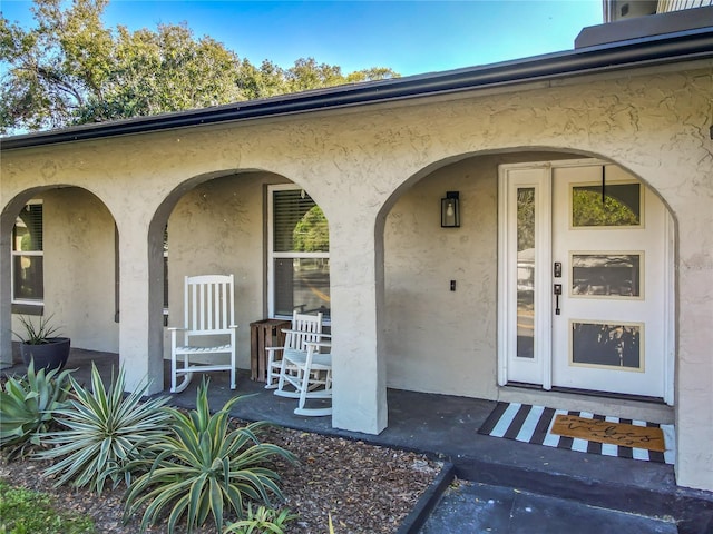 entrance to property with a porch and stucco siding