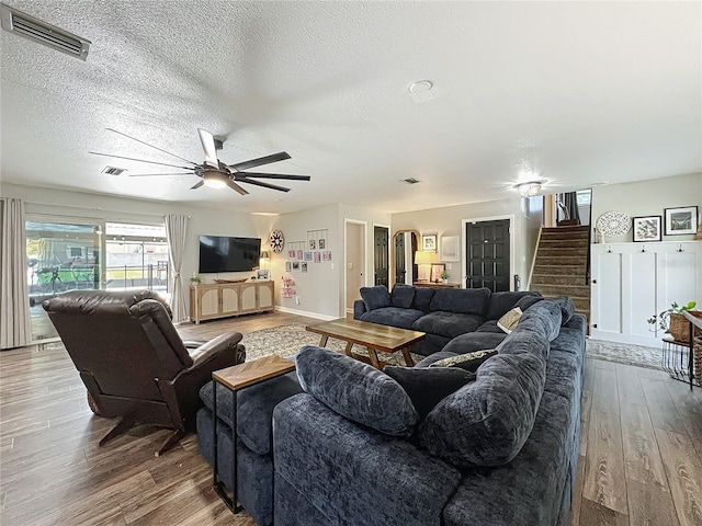 living room featuring stairs, ceiling fan, wood finished floors, and visible vents