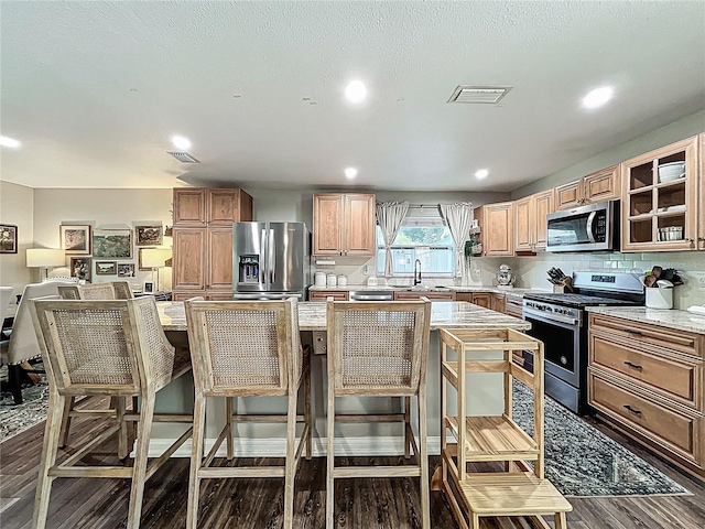 kitchen featuring visible vents, dark wood-type flooring, stainless steel appliances, a kitchen bar, and a sink