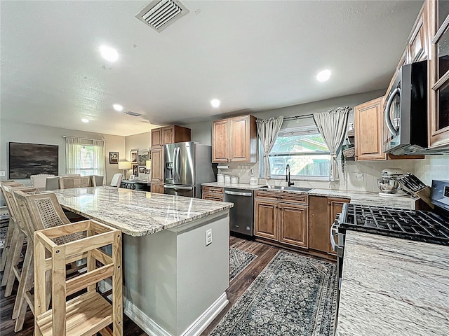 kitchen with visible vents, light stone counters, a breakfast bar area, stainless steel appliances, and a sink