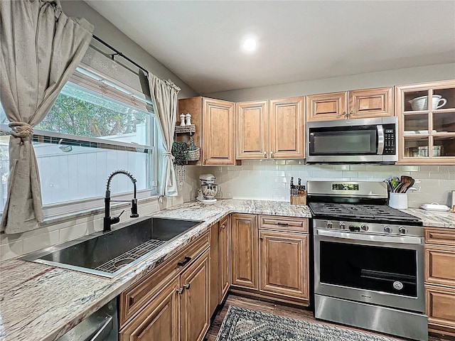 kitchen featuring a sink, appliances with stainless steel finishes, light stone countertops, tasteful backsplash, and glass insert cabinets