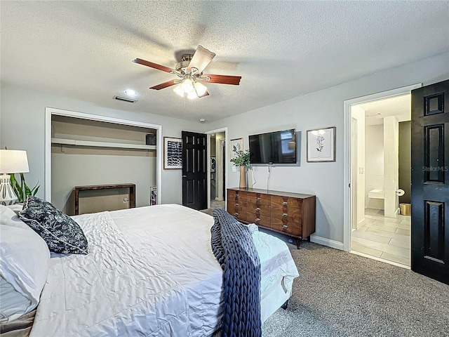 carpeted bedroom with a textured ceiling, ceiling fan, visible vents, a closet, and ensuite bath