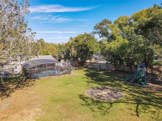 view of yard featuring glass enclosure, a fenced backyard, and a playground