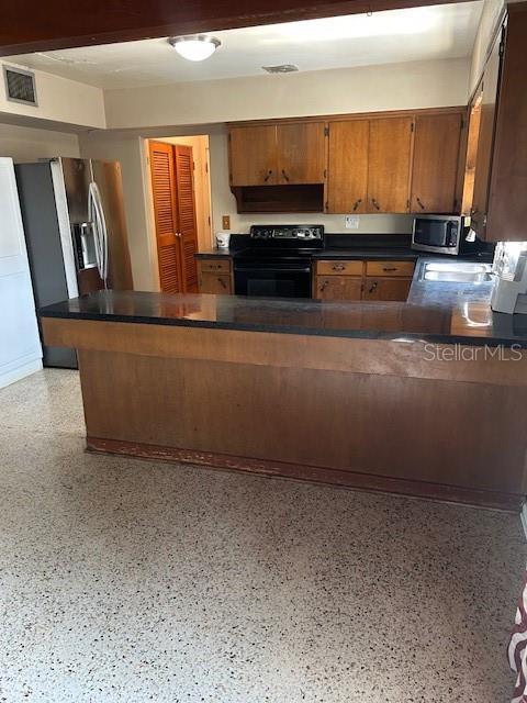 kitchen featuring dark countertops, visible vents, brown cabinetry, stainless steel appliances, and speckled floor