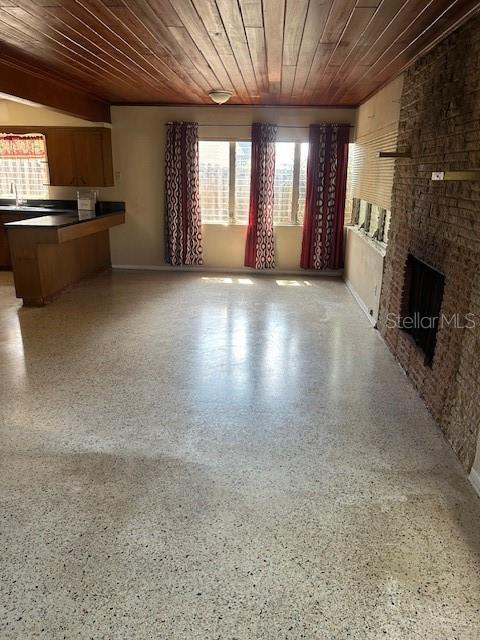 unfurnished living room featuring a brick fireplace, wood ceiling, speckled floor, and a sink