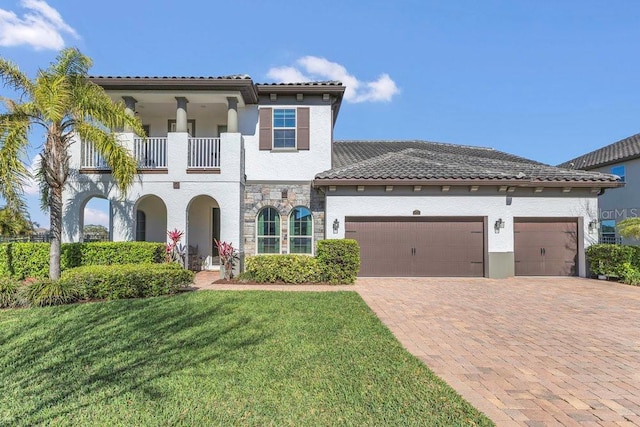 mediterranean / spanish home with a front yard, a balcony, stucco siding, a garage, and decorative driveway