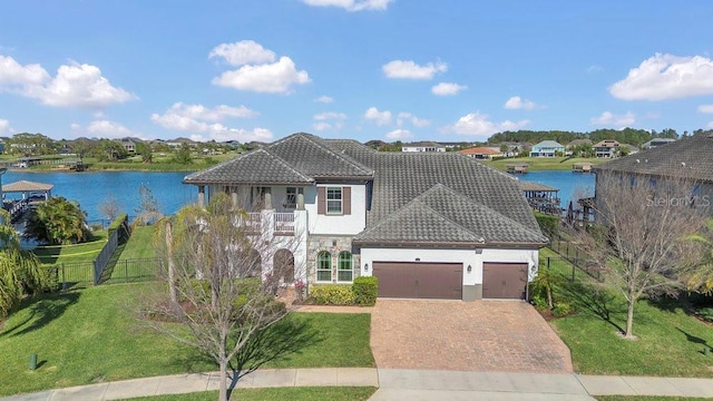 view of front facade featuring stucco siding, a water view, a front lawn, an attached garage, and a tiled roof