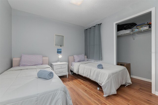 bedroom with a spacious closet, a closet, wood finished floors, and baseboards