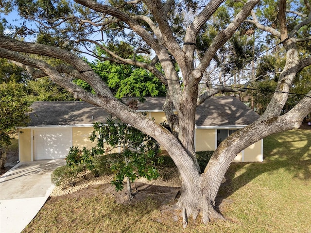 view of front facade with stucco siding, driveway, roof with shingles, a front yard, and a garage