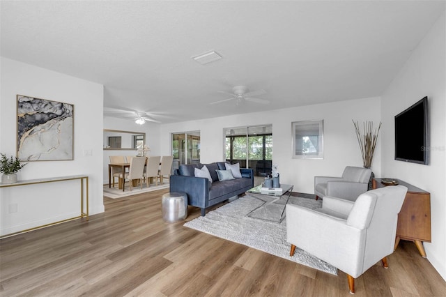 living area with a ceiling fan, wood finished floors, visible vents, and baseboards