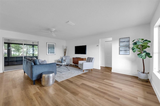 living room featuring ceiling fan, a textured ceiling, baseboards, and light wood-style floors