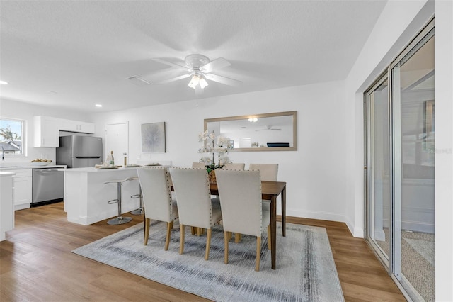 dining space featuring ceiling fan, baseboards, light wood-type flooring, recessed lighting, and a textured ceiling