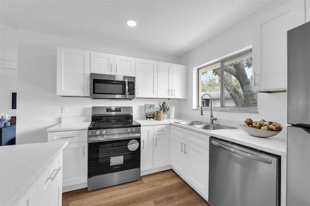 kitchen with a sink, light countertops, white cabinets, light wood-style floors, and appliances with stainless steel finishes