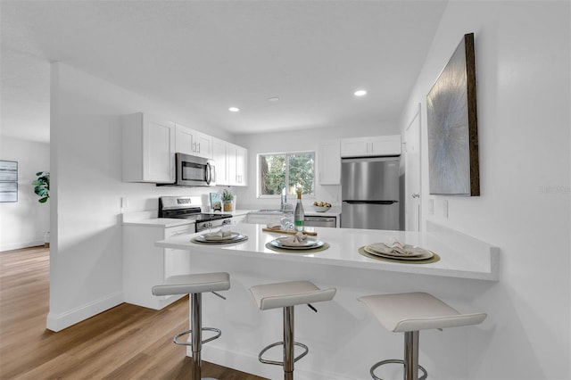 kitchen featuring light countertops, a kitchen breakfast bar, appliances with stainless steel finishes, a peninsula, and white cabinets