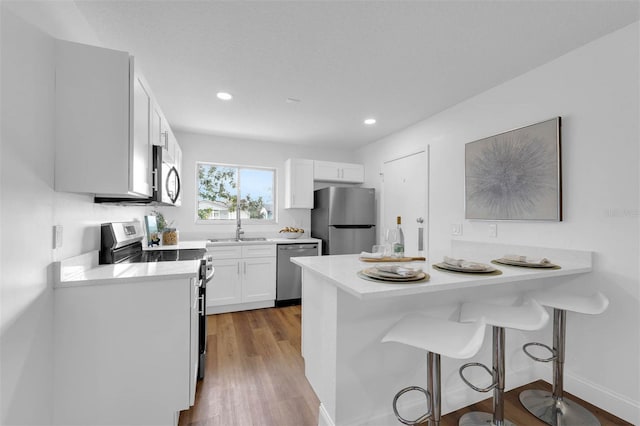 kitchen with a breakfast bar, wood finished floors, a peninsula, appliances with stainless steel finishes, and white cabinets