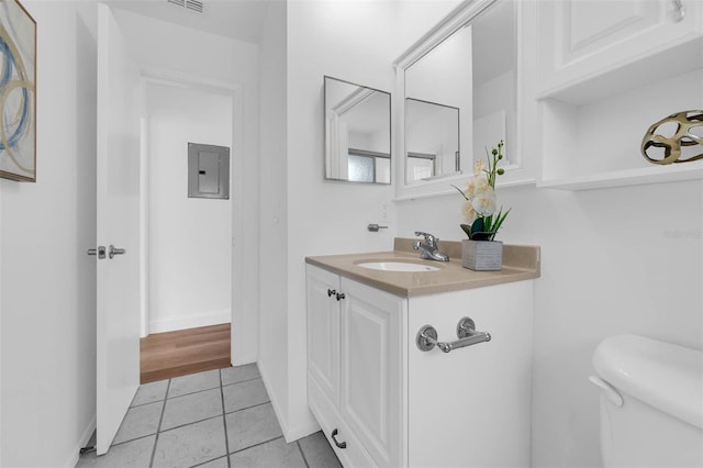 half bath with toilet, electric panel, tile patterned flooring, baseboards, and vanity