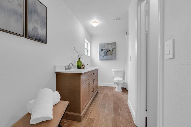 bathroom with visible vents, baseboards, wood tiled floor, toilet, and double vanity