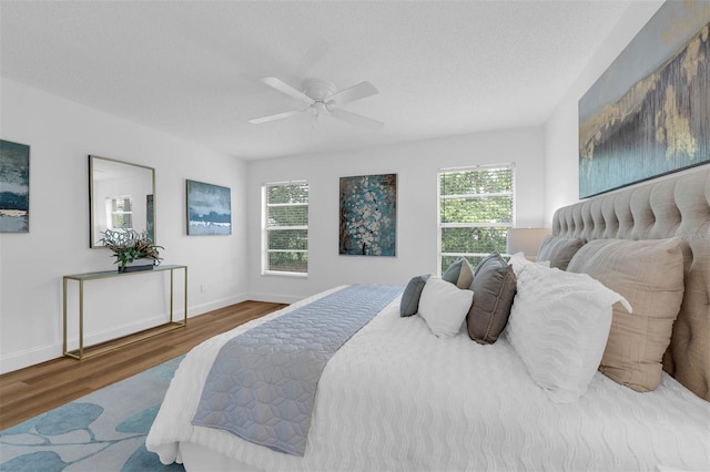 bedroom with baseboards, multiple windows, a textured ceiling, and wood finished floors