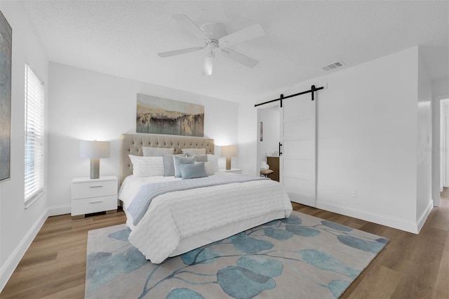 bedroom featuring a barn door, wood finished floors, visible vents, and a textured ceiling