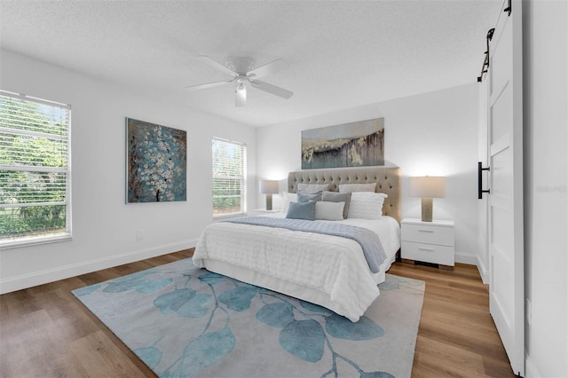 bedroom featuring baseboards, a barn door, wood finished floors, a textured ceiling, and a ceiling fan