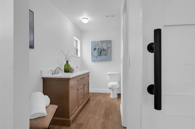 bathroom featuring vanity, wood finished floors, visible vents, baseboards, and toilet