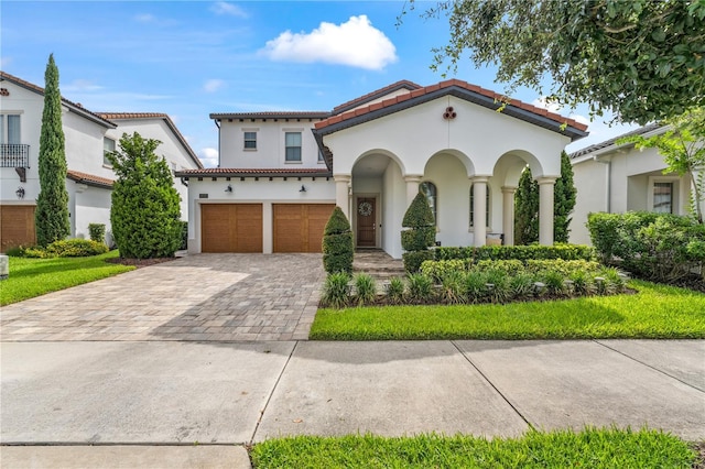 mediterranean / spanish-style house with a garage, a tiled roof, decorative driveway, and stucco siding