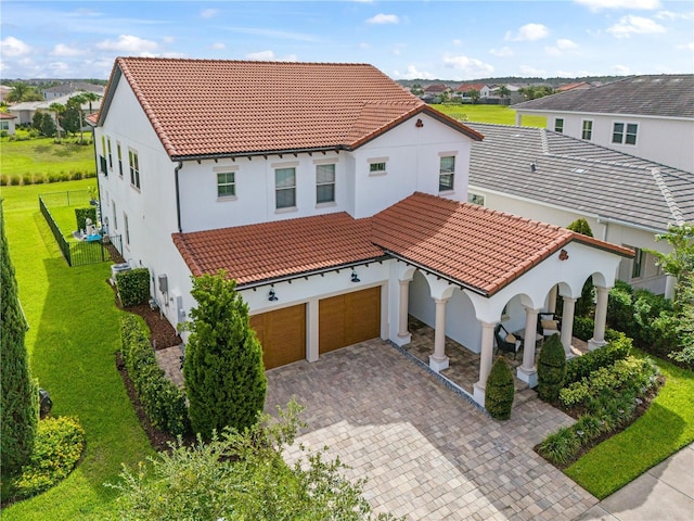 mediterranean / spanish-style home with a front lawn, decorative driveway, a tile roof, and stucco siding