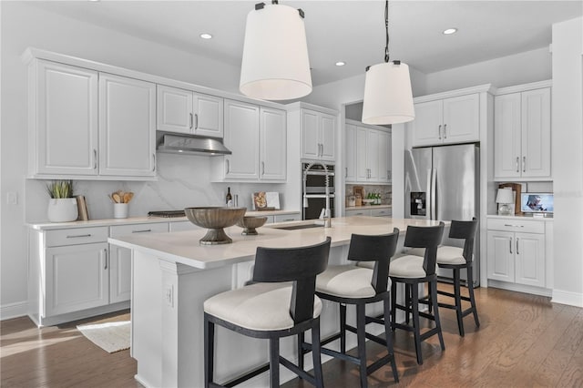 8025 Topsail Pl, Winter Garden, FL 34787 - kitchen with appliances with stainless steel finishes, a center island with sink, under cabinet range hood, light countertops, and dark wood-style flooring
