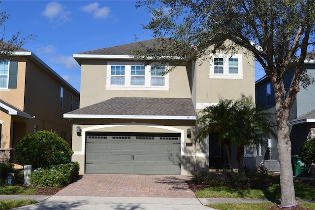 view of front of home featuring roof with shingles, decorative driveway, an attached garage, and stucco siding