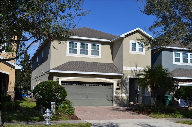 view of front of property featuring a shingled roof, decorative driveway, a garage, and stucco siding