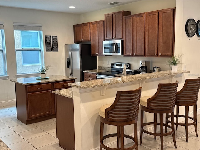 kitchen with a center island, a peninsula, stainless steel appliances, a kitchen bar, and light tile patterned flooring