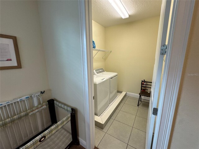 clothes washing area featuring light tile patterned floors, washing machine and dryer, a textured ceiling, laundry area, and baseboards
