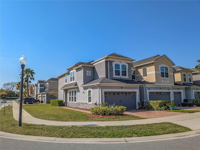 view of front of home with decorative driveway, stucco siding, an attached garage, a front yard, and a residential view