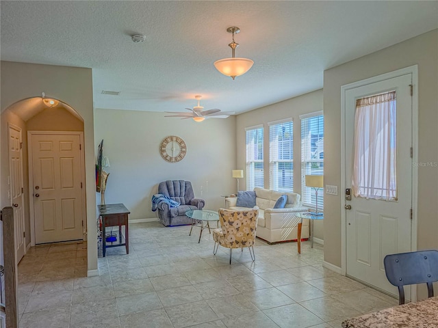 interior space with arched walkways, visible vents, ceiling fan, a textured ceiling, and baseboards