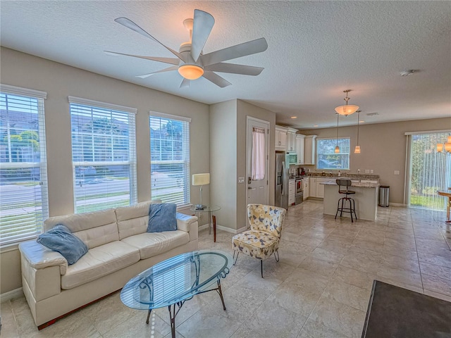 living area with ceiling fan, a textured ceiling, and baseboards