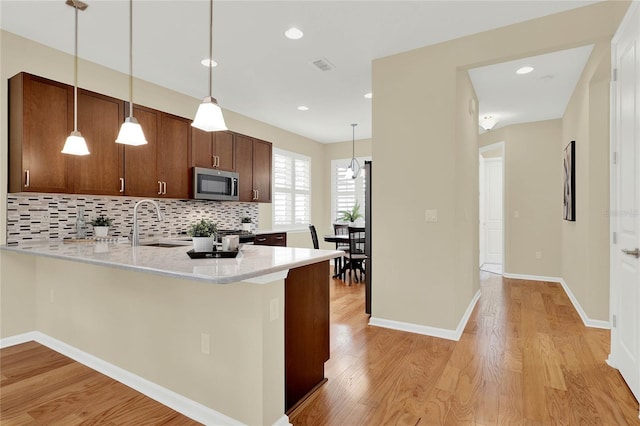 kitchen featuring light wood-style flooring, decorative light fixtures, stainless steel microwave, backsplash, and a peninsula