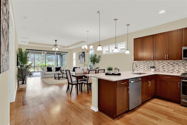 kitchen featuring a sink, a tray ceiling, open floor plan, stainless steel appliances, and a peninsula