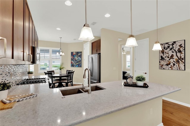 kitchen with a sink, wood finished floors, appliances with stainless steel finishes, a peninsula, and light stone countertops