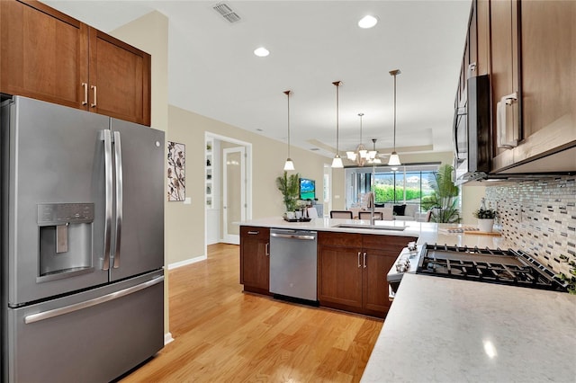 kitchen featuring a sink, stainless steel appliances, light wood-style floors, light countertops, and decorative backsplash