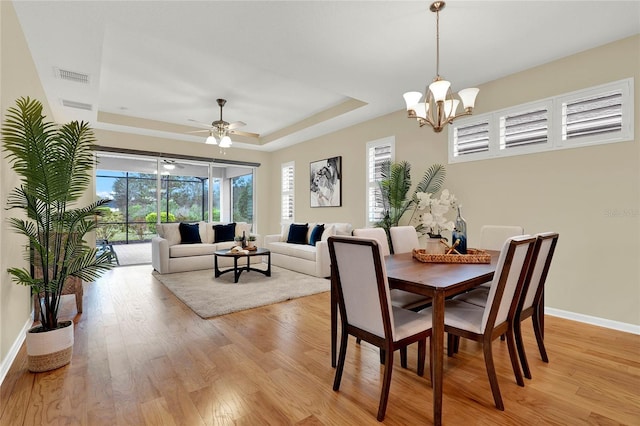 dining space with a tray ceiling, light wood-style floors, visible vents, and baseboards