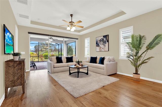 living room with a raised ceiling, wood finished floors, and visible vents