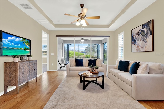 living area featuring a tray ceiling, baseboards, visible vents, and light wood-type flooring