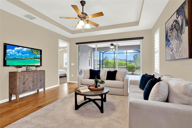 living room featuring light wood-style flooring, baseboards, and a tray ceiling